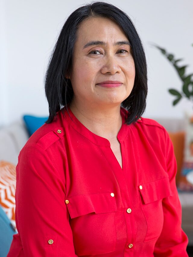 Headshot of woman wearing fuchsia top with a sofa and decorative pillows in the background.