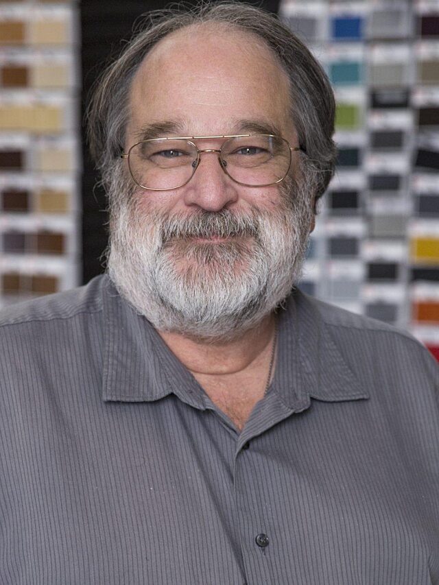 Headshot of a man wearing a gray shirt with a colorful swatch wall in the background.