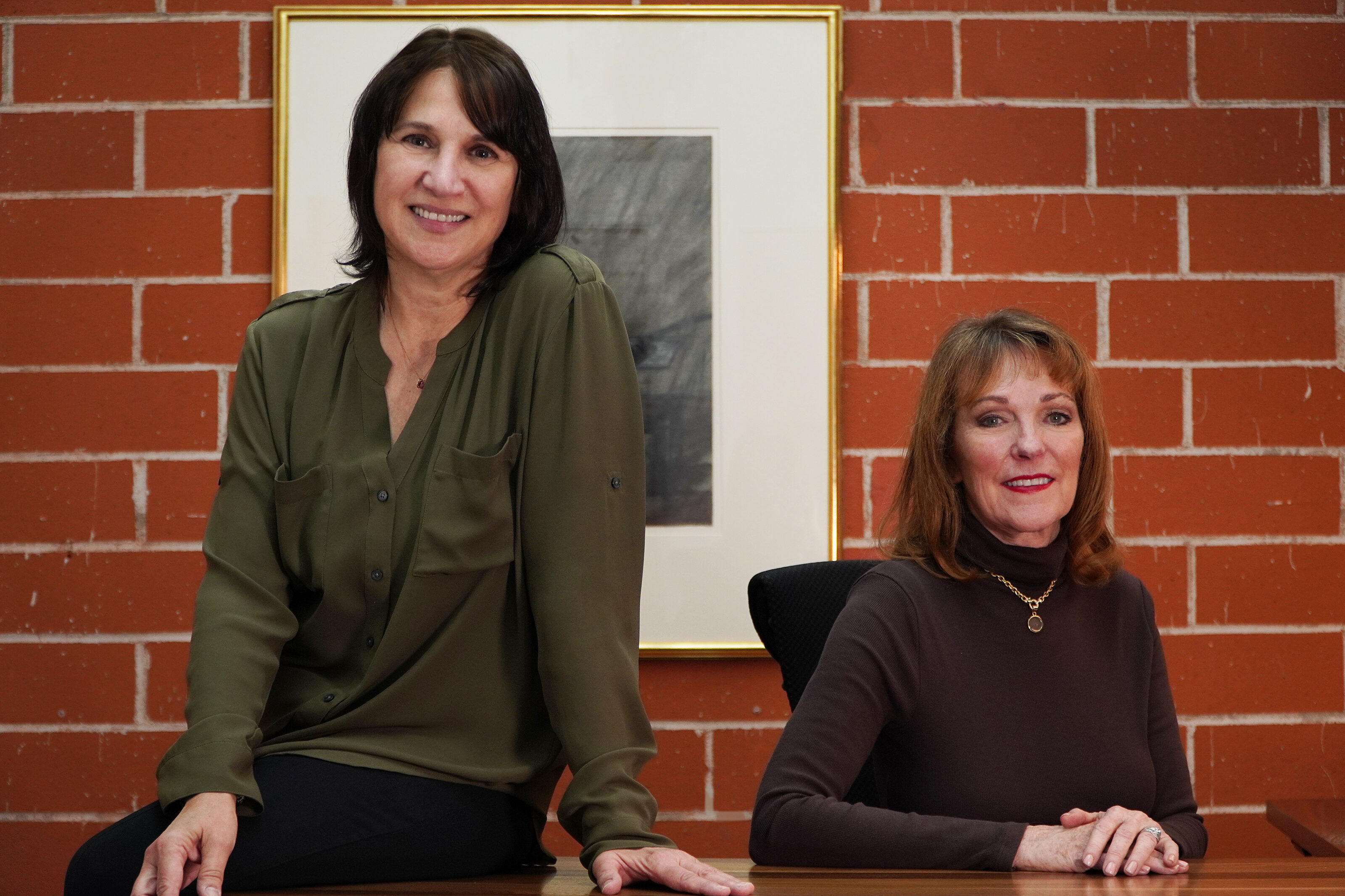 Two women posing in an office, smiling at the camera.