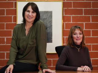 Two women posing in an office, smiling at the camera.