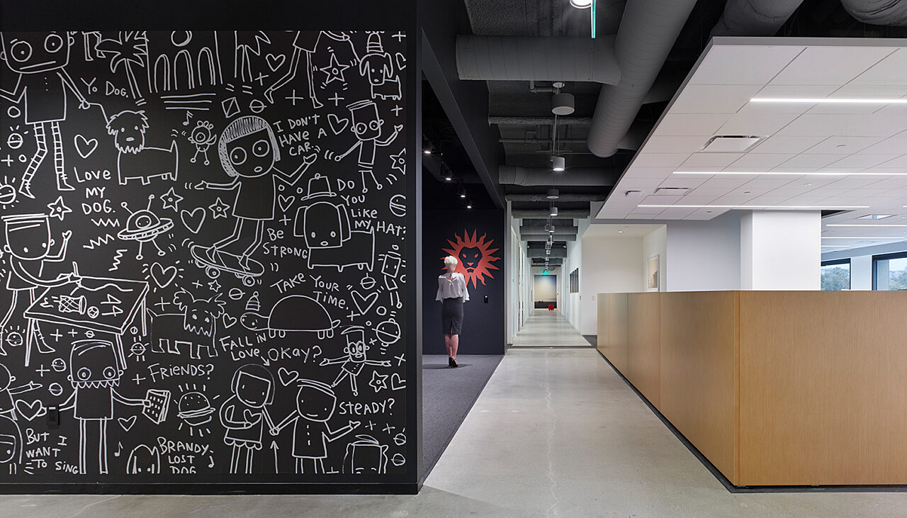 A unique cartoon wall runs parallel to the wooden partition dividing workstations and the hallway, adding a playful touch to the space.