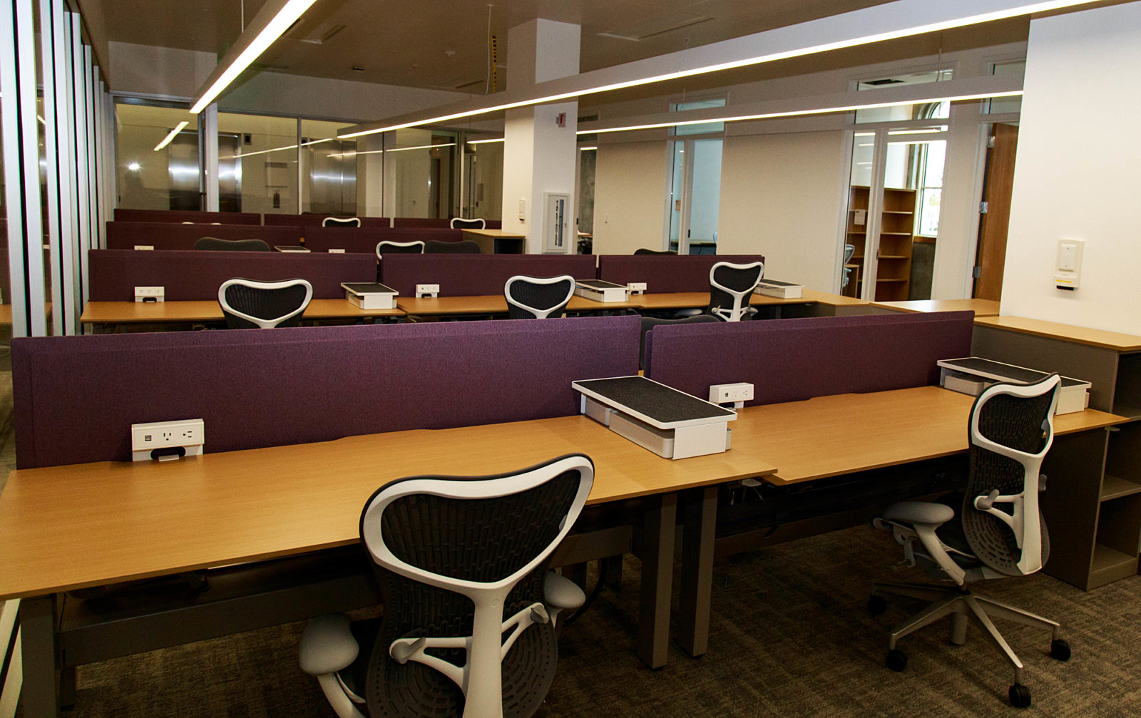 A workplace with numerous workstations, each equipped with a hardwood desk and an executive-style chair.