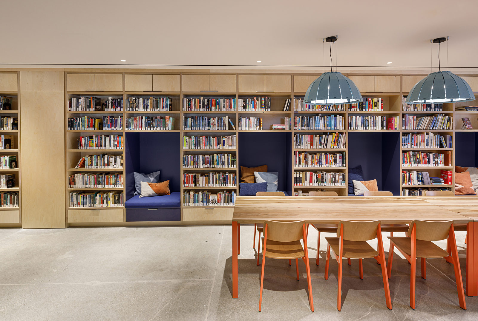 An open space with custom wooden bookshelf booths and a large meeting table surrounded by six chairs. Perfect for reading and meetings.