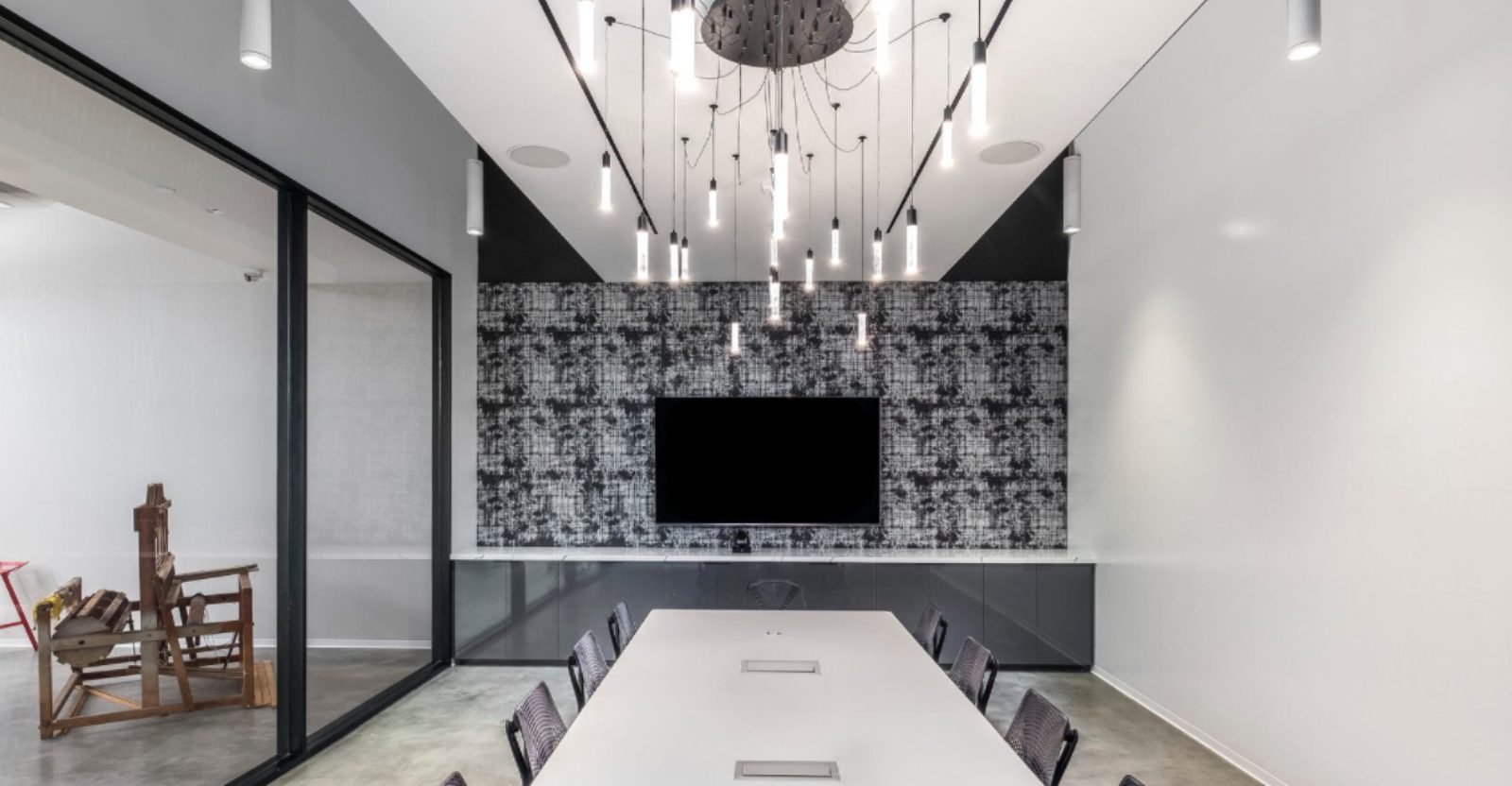 Stylish meeting room: white conference table, screen wall backdrop, and elegant chandelier illuminating the space.