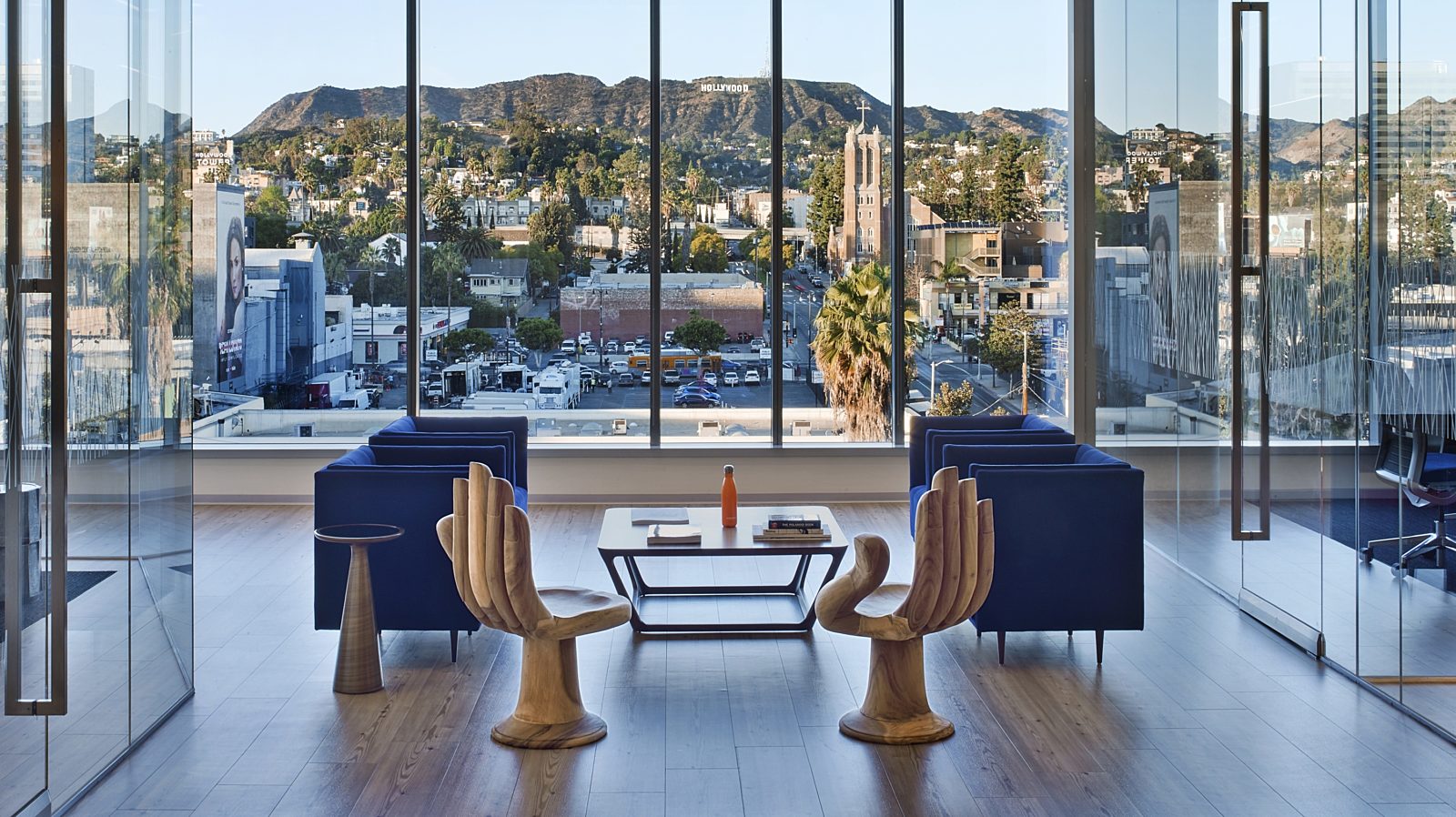 A lounge space in front of glass walls that reveal a distant view of the Hollywood hills. The lounge space features two chairs that resemble hands.