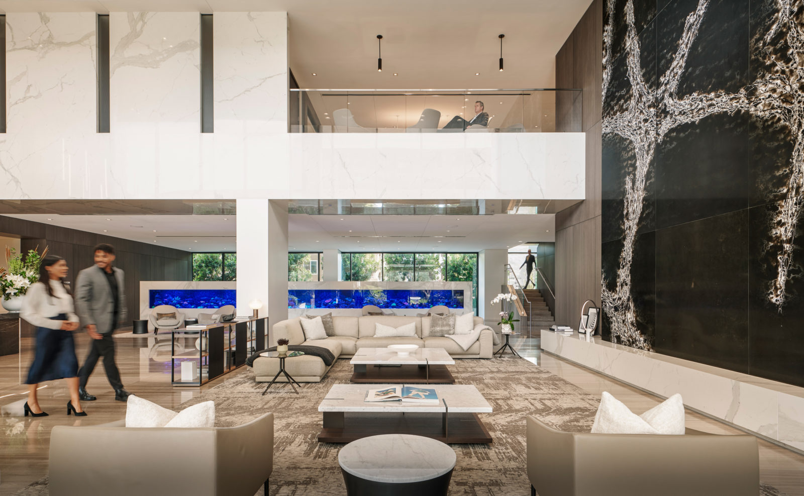 A white leather sofa and two coffee tables are flanked by two lounge chairs in the foyer. A two-story-high artwork serves as a magnificent backdrop.