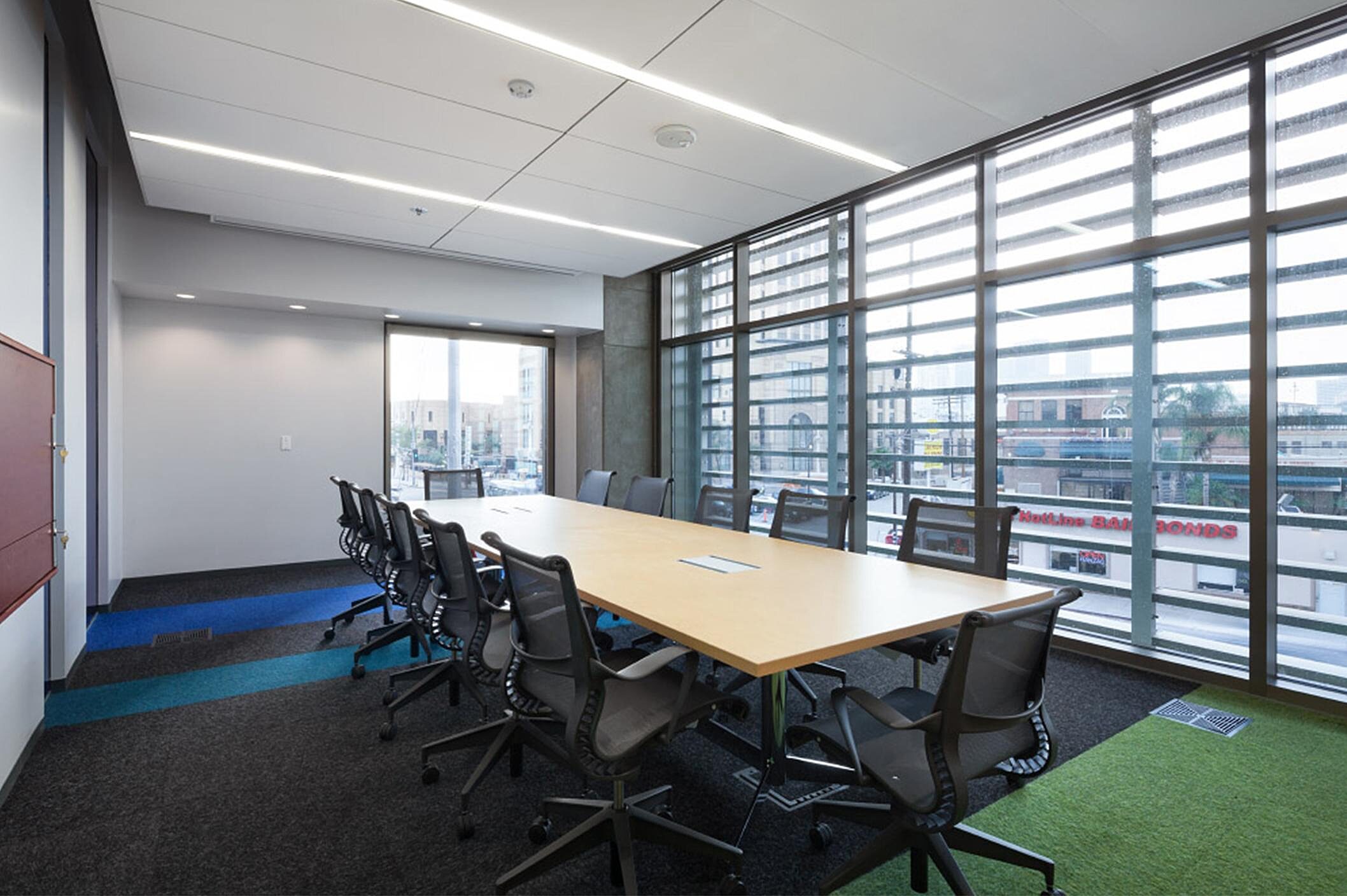 In a conference room, there is a wooden conference table and several black office chairs.