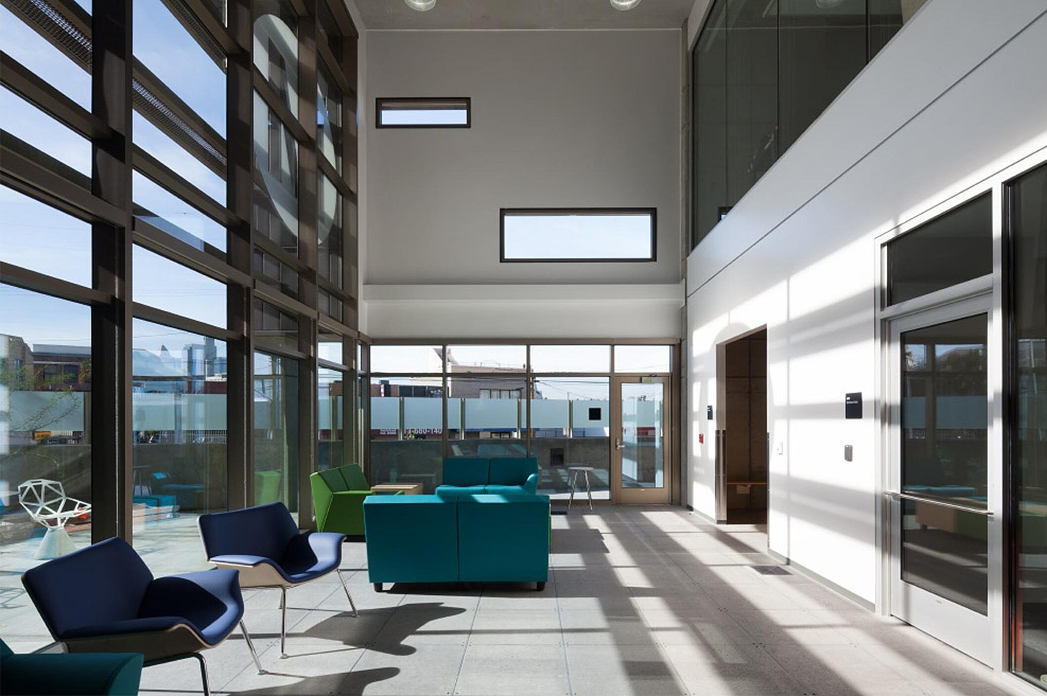 In a public area, there are blue and green sofas and blue wing chairs on the side.