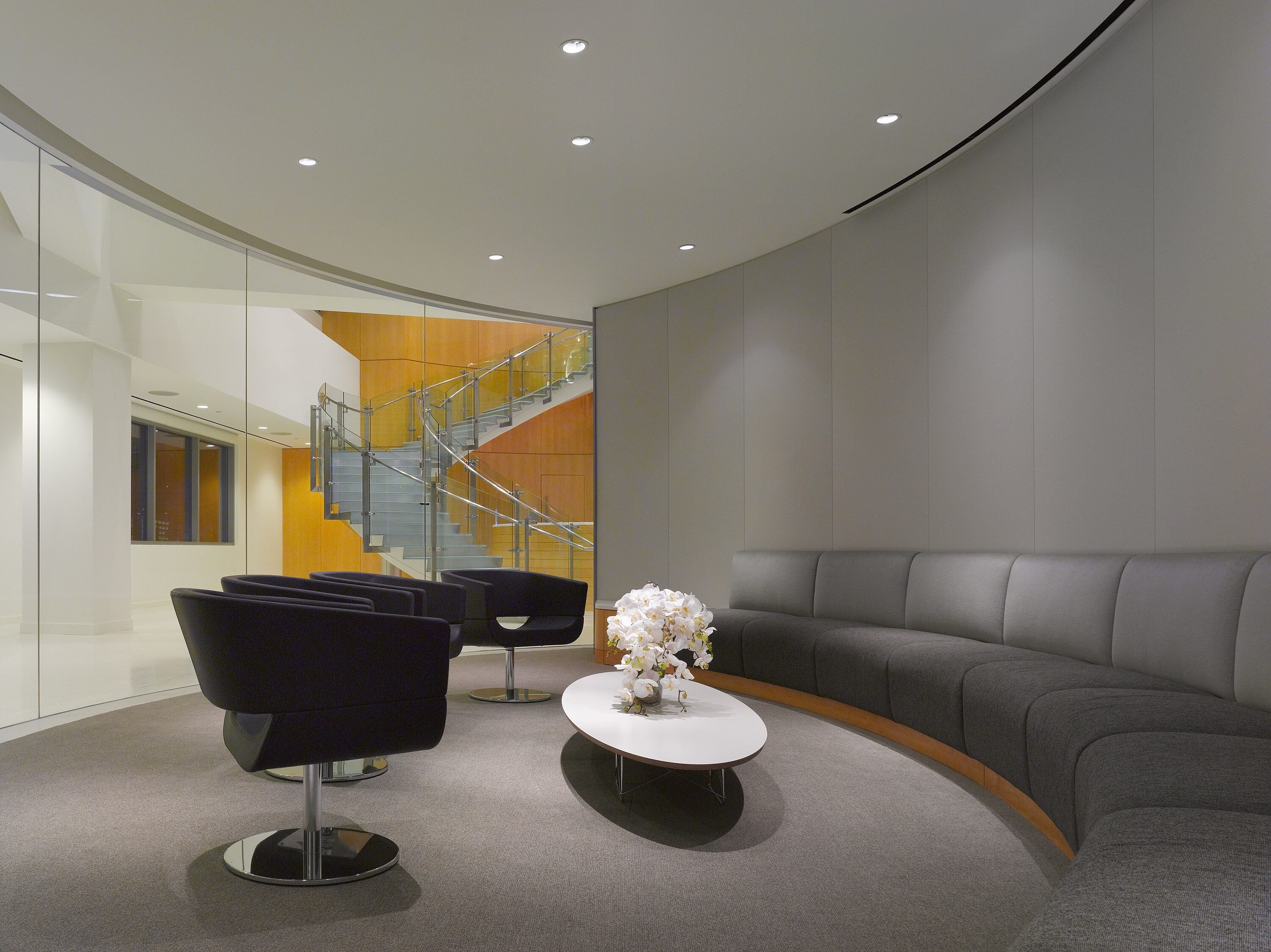A private room with a round settee placed against the wall, several black lounge chairs, and a white coffee table in the center.