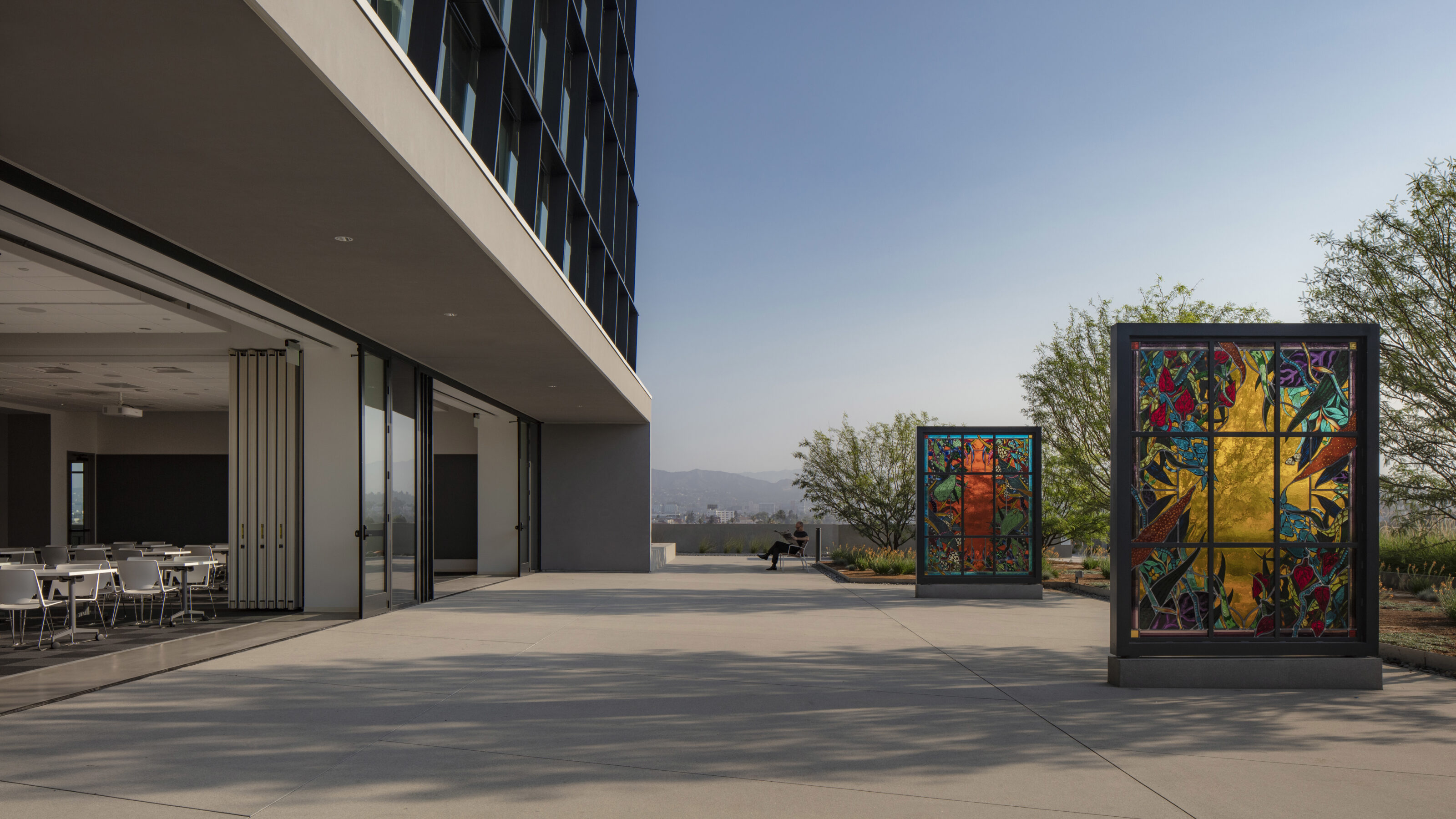 Colorful windows frame lush trees in a spacious outdoor space adjacent to the assembly room, set against a gorgeous open sky backdrop.