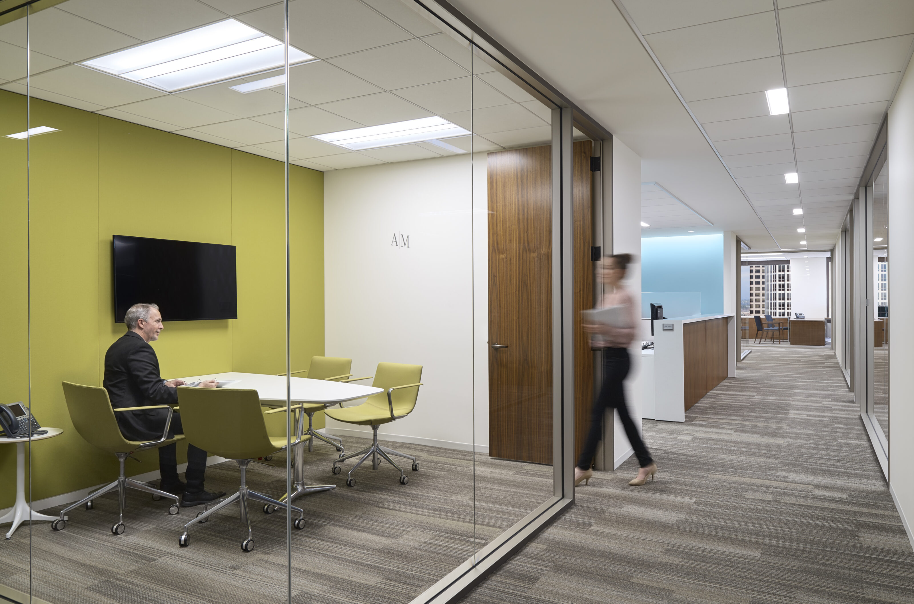 A private office adjacent to the hallway, furnished with a white conference desk and complemented by vibrant yellow office chairs.