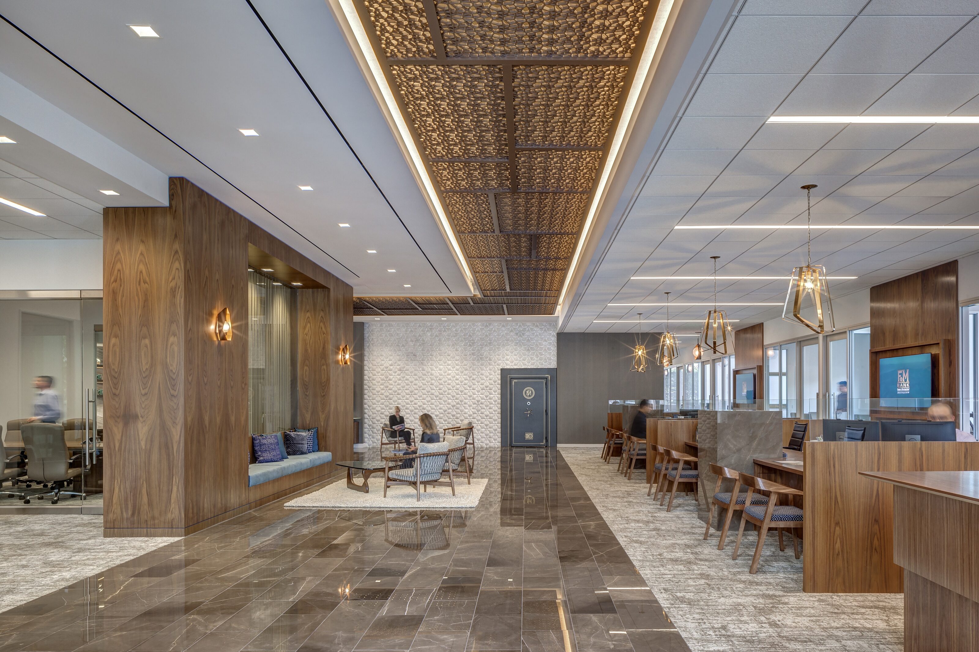 In an open area, there are wooden office desks and chairs with wooden partition in between. There's also a wooden made lounges and glass surface cafe table
