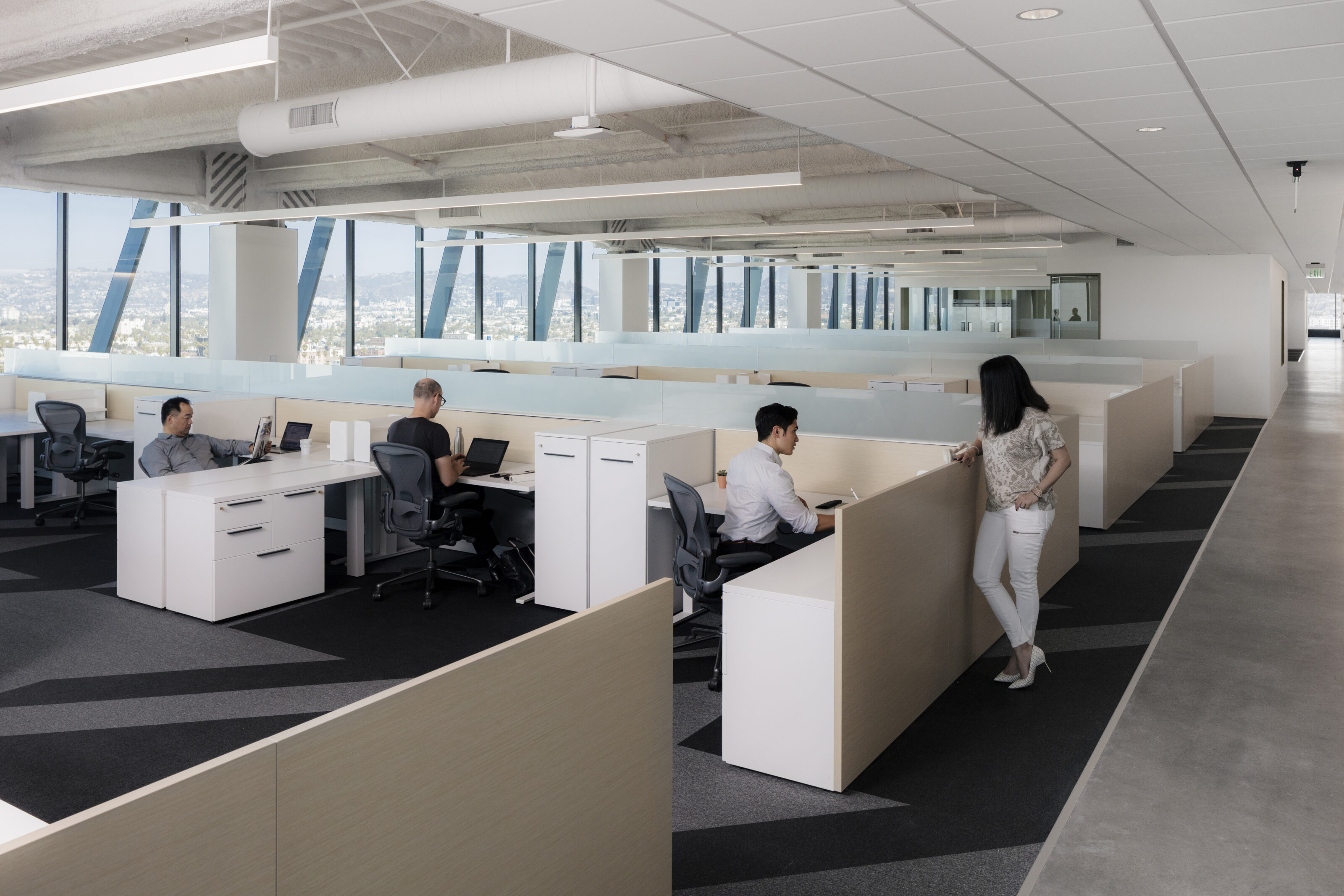 Individual workstations are set up with wooden walls in a room with French windows that look out on a beautiful view of the city.