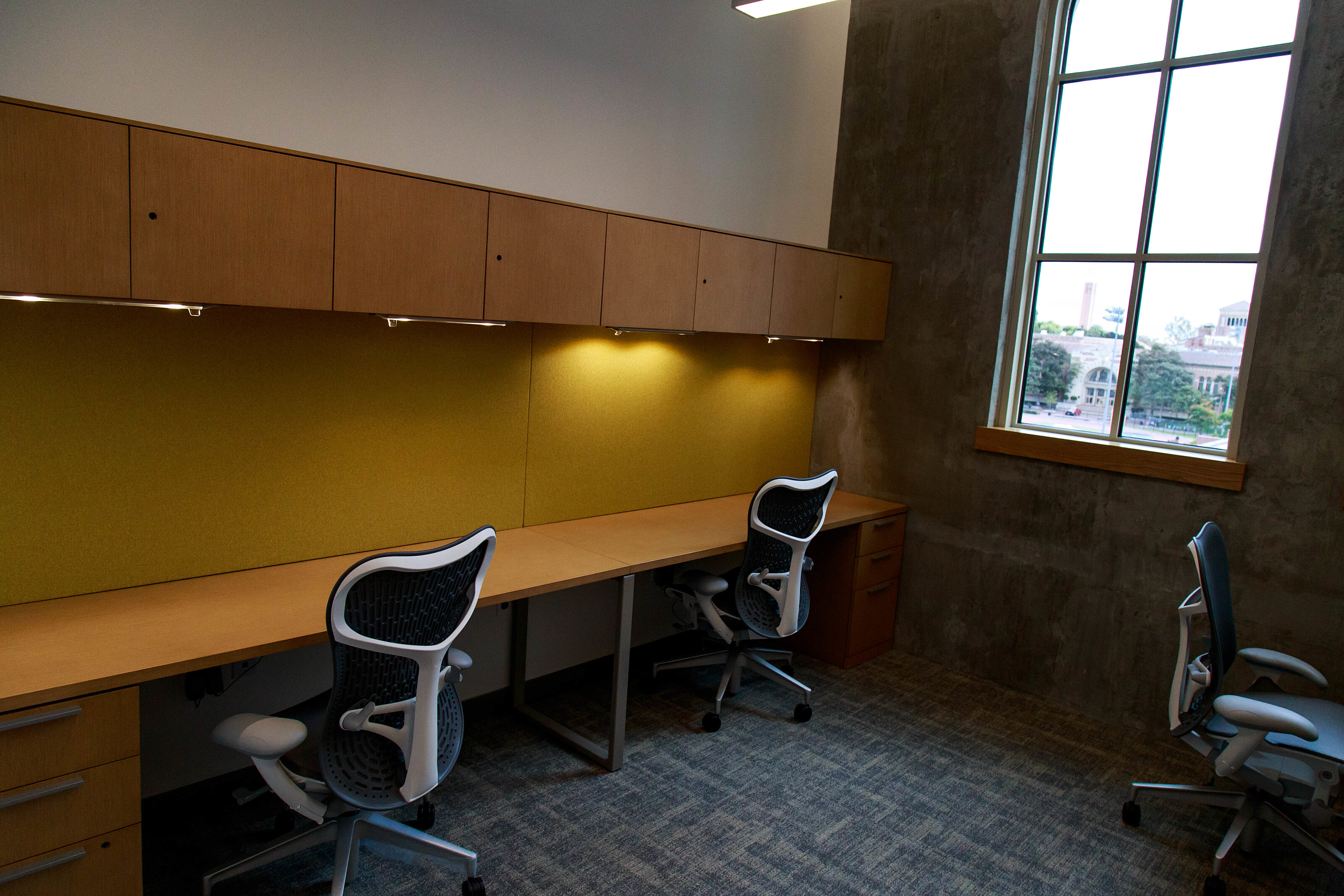 Many study stations have mahogany desks and executive chairs. The desks are next to a stunning series of French windows.