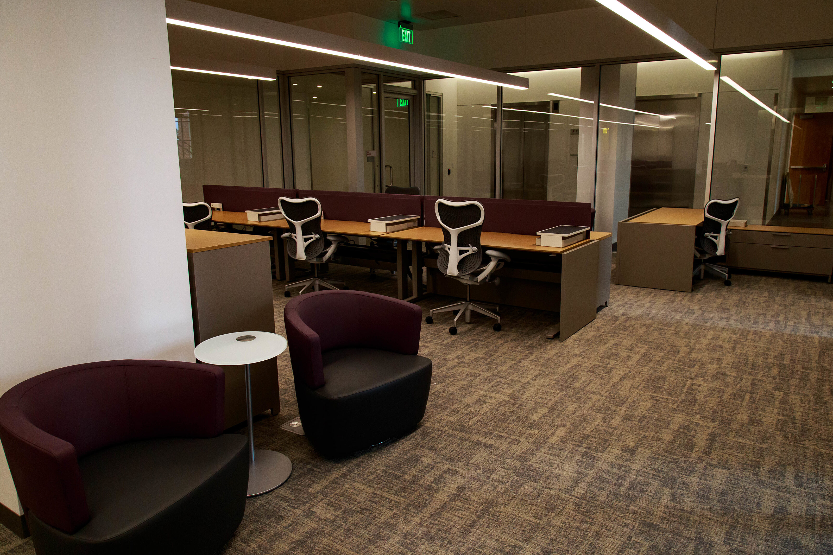 An office that contains many workstations, each of which is furnished with a wooden desk and a chair suitable for an executive.