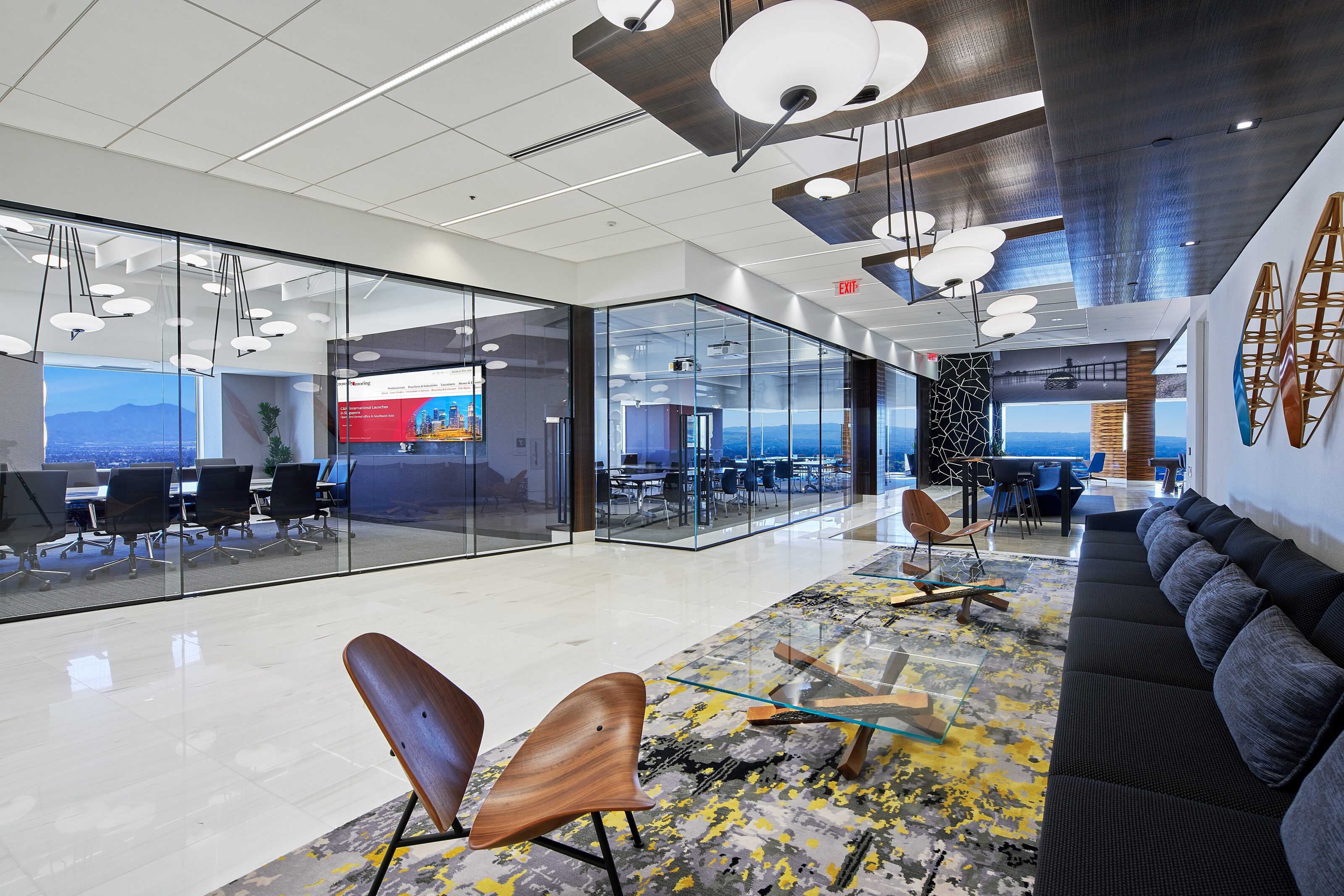 In a open area, there is a long black cotton sofa, wooden chair, glass surface cafe table, and a conference table.