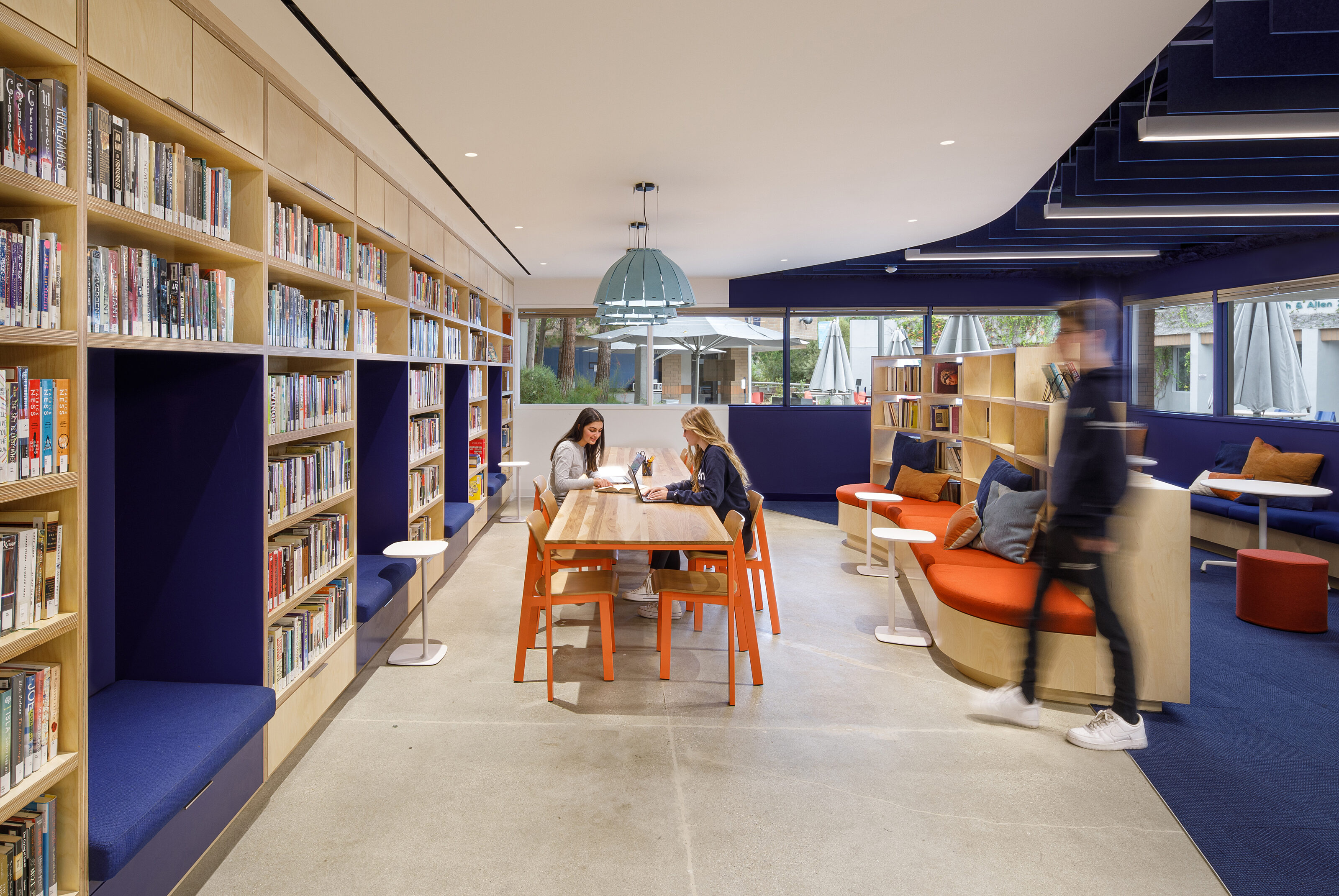 The open reading room contains lounge seats, coffee tables, handmade bookshelf booths, and a dark blue carpet.