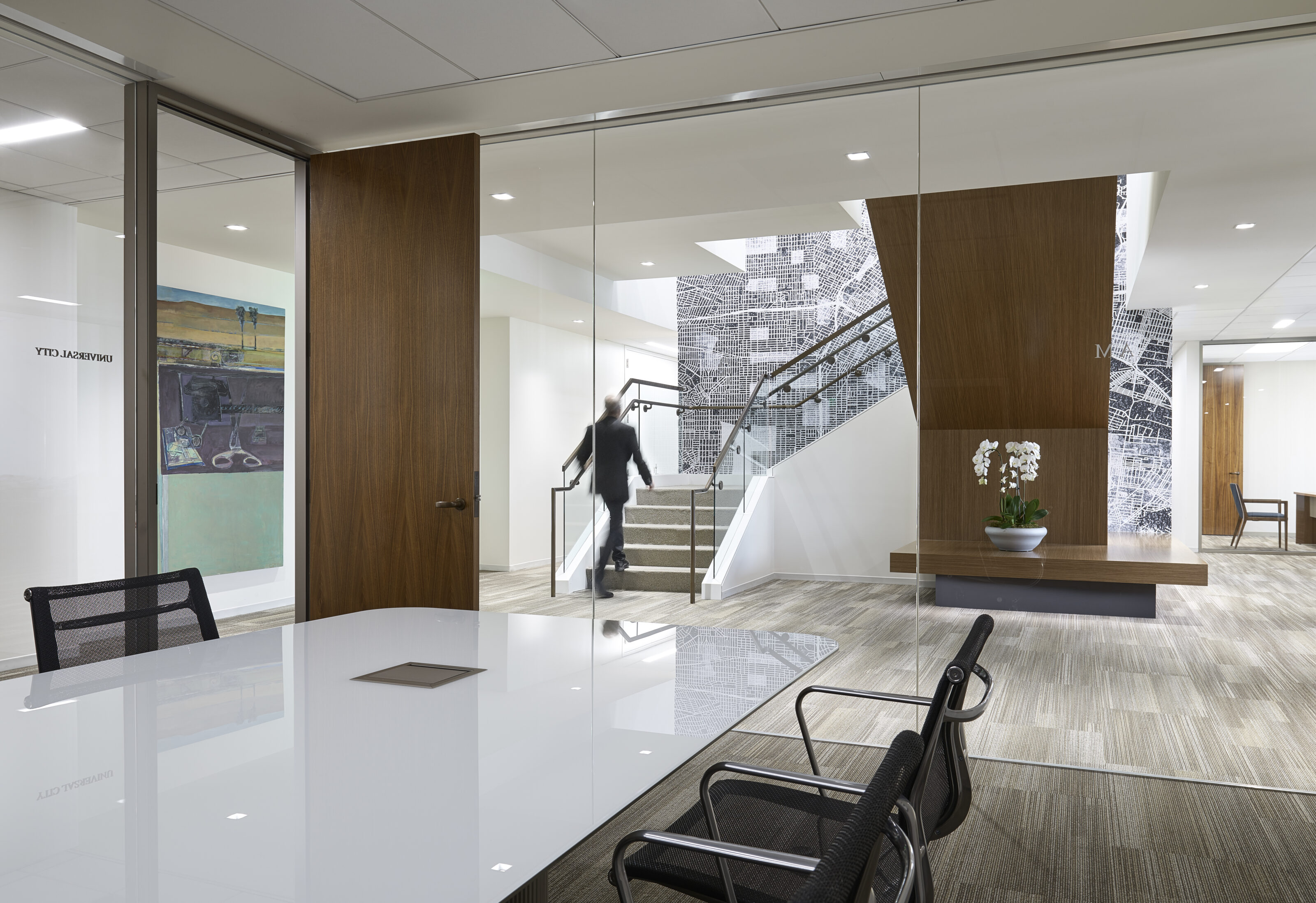 A private conference room with a white conference desk and black office chairs, featuring glass walls and a wooden door for a modern, sophisticated look