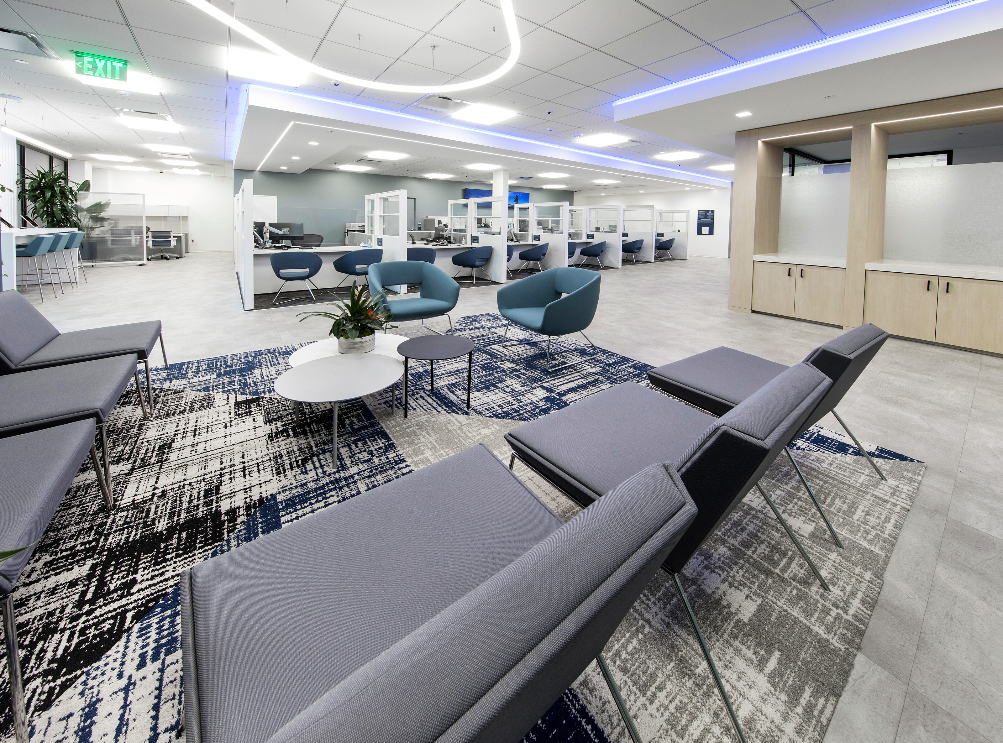 The opposite angle from the corner at the bank counters. A small waiting area with two gray lounge chairs arranged around a coffee table.