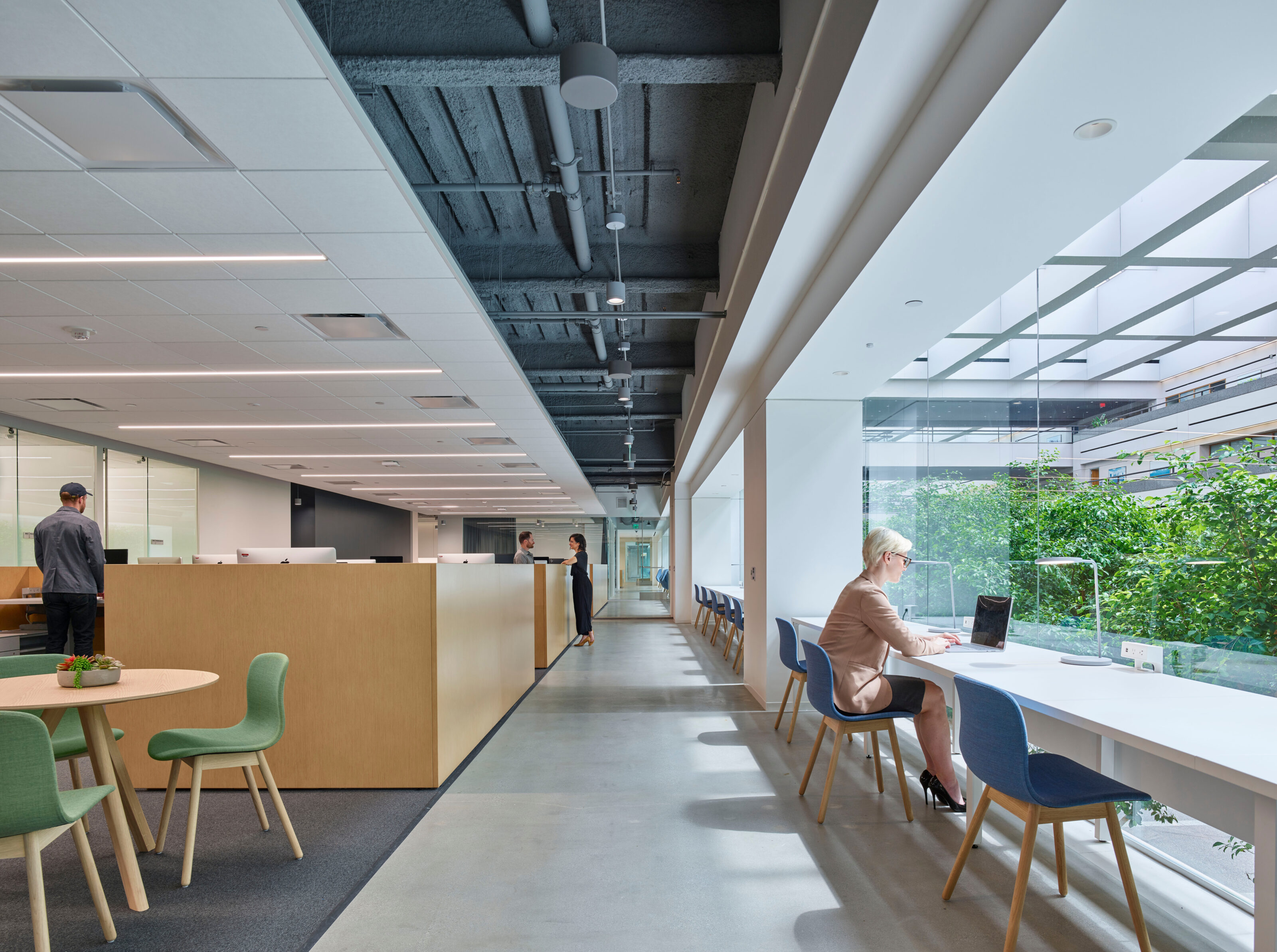 A diverse workspace on a college campus. Round tables with chairs to collaborate, independent desks for focused work and tables lining an open window.