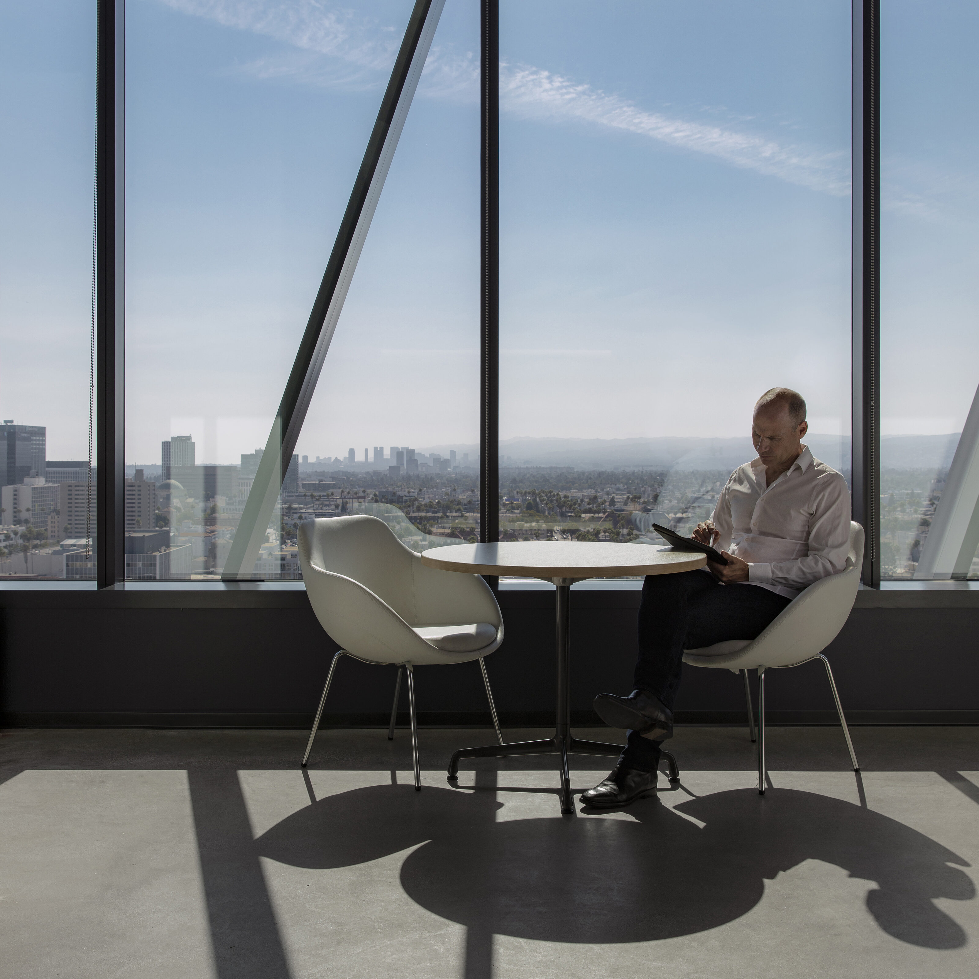 Next to the large French window is a Café table and two white lounge chairs. A man is concentrating on his iPad.