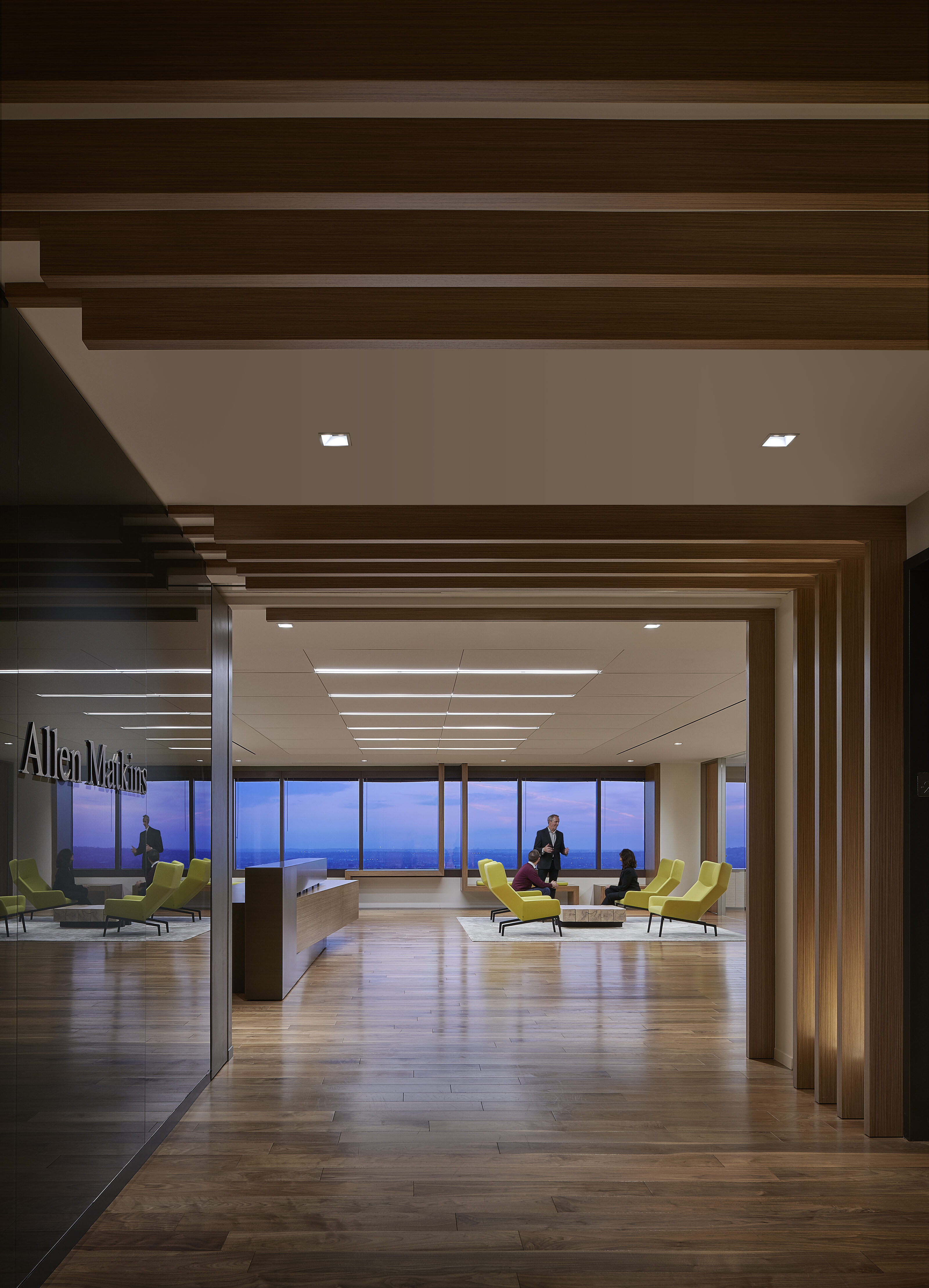 A hallway featuring inviting yellow lounge chairs in the waiting area, culminating in a window that offers a breathtaking nighttime view.