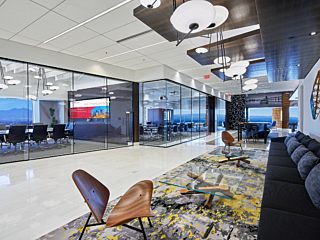 In a open area, there is a long black cotton sofa, wooden chair, glass surface cafe table, and a conference table.