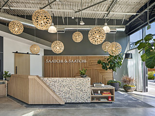 Modern reception desk against wooden wall backdrop, bright with natural light and surrounded by lush plants.