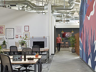 A spacious open office with numerous ergonomic chairs and wooden conference tables at the workstations.