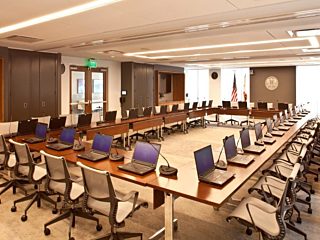 An assembly room with a square-shaped wooden conference desk at the center, encircled by office chairs for collaborative discussions and meetings.