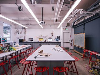Classroom with long gray bar-height tables accompanied by sculptural Magis stool with a red finish.