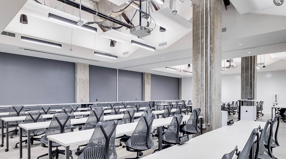 Light assembly room with rows of conference tables and ergonomic chairs for productive meetings.