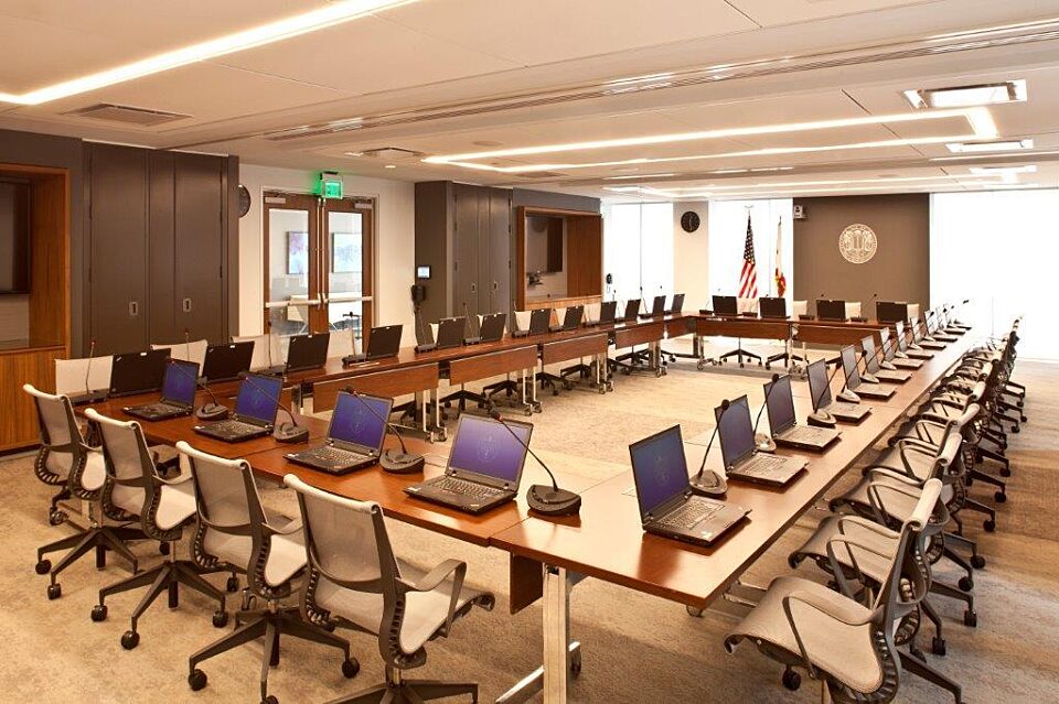 An assembly room with a square-shaped wooden conference desk at the center, encircled by office chairs for collaborative discussions and meetings.