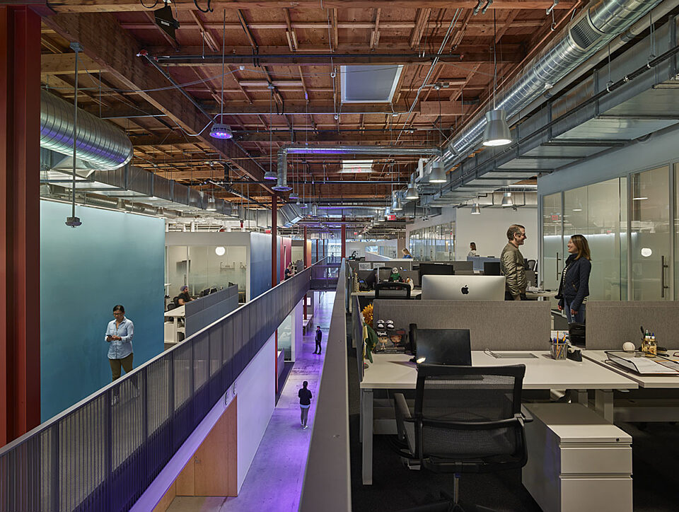 There are white office desks and black office chairs with a white drawers on second floor open area.